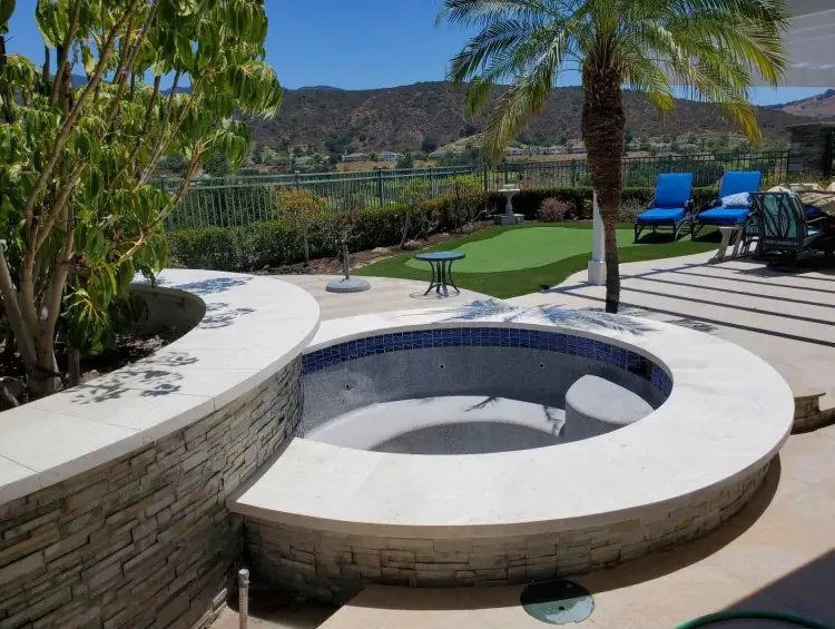 Curved in-ground spa with stone veneer wall and landscaped pool area
