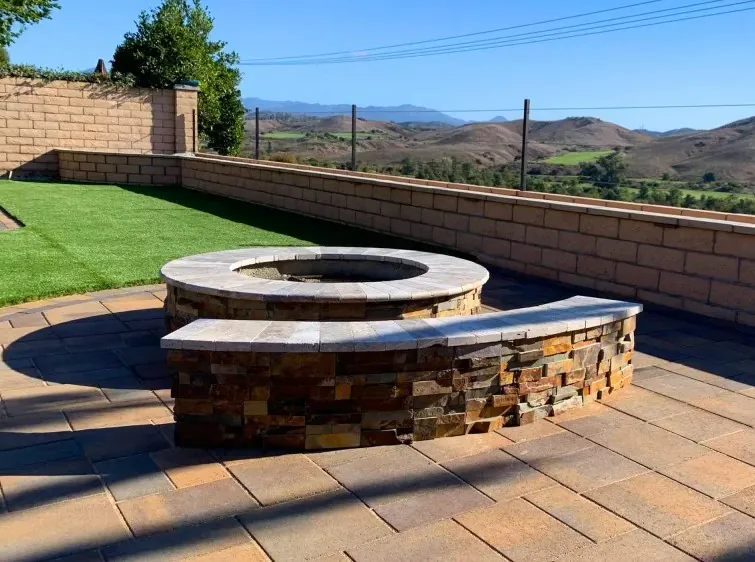 Round custom stone fire pit with curved masonry seating wall and pavers